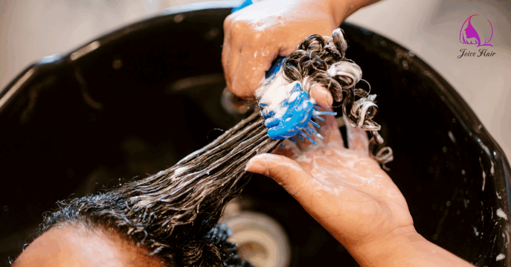 Stylist deep conditioning and detangling curly bulk hair for braiding at a salon sink.